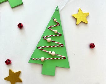 Può includere: Ornamento per albero di Natale in legno verde con dettagli in spago rosso e bianco, perline di legno e un cordino bianco per appenderlo. Stelle dorate e campane rosse.