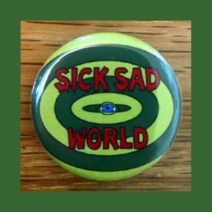 May include: A green and yellow button with a red and white eye in the center. The text "Sick Sad World" is written in red letters around the eye.