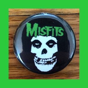 以下が含まれることがあります： 緑色の「Misfits」ロゴと黒い目の白いドクロが描かれた黒と白のボタン