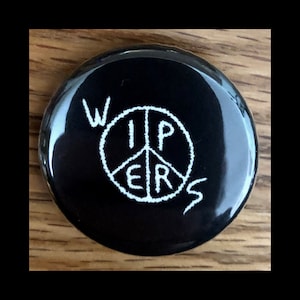 May include: Black button with a white peace sign and the word "Wipers" written around it.