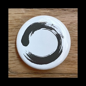 Könnte beinhalten: Ein weißer Knopf mit einem schwarzen Kreisdesign aus Pinselstrichen. Der Kreis ist unvollständig und bildet ein Zen-Symbol.