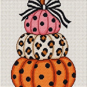 May include: A cross-stitch pattern featuring a stack of three pumpkins. The top pumpkin is pink with black polka dots, the middle is white with a brown leopard print, and the bottom is orange with black polka dots. A black and white striped bow sits on top.