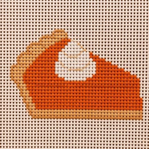 May include: A needlepoint canvas featuring a single slice of pumpkin pie with a dollop of white whipped cream on top. The pie slice has a bright orange filling and a light tan crust, all stitched onto a white grid mesh background.