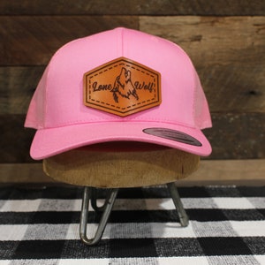 May include: Pink trucker hat with a brown leather patch that says "Lone Wolf" and features a wolf howling at the moon.