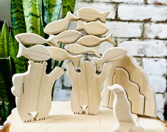 May include: Wooden toy set featuring two polar bears, a penguin, and a school of fish. The bears are holding up the fish, which are stacked on top of each other. The penguin is standing on a wooden base, which is shaped like a piece of driftwood. The set is made of natural wood and is perfect for imaginative play.