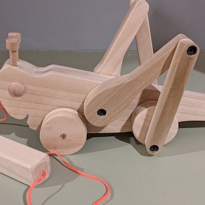 May include: A wooden pull toy shaped like a grasshopper with a red string attached. The toy has two wheels and a movable head and legs.