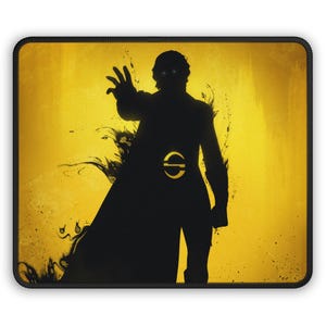 May include: A rectangular mouse pad featuring a black silhouette of a figure with glowing white eyes against a vibrant yellow background. The figure has one arm extended forward and displays a circular emblem on the chest area with a black border.