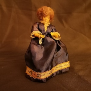 May include: A vintage doll with brown hair wearing a dark blue dress with gold trim. The doll is holding a small gold key.
