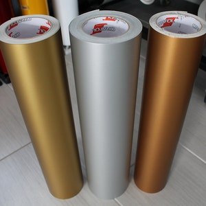 May include: Three rolls of adhesive vinyl in gold, silver, and copper colors. Each roll is labeled "GRAFOL" and has a white core.
