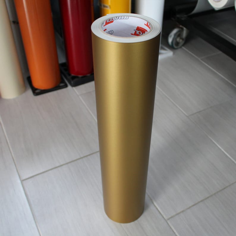 May include: A roll of gold vinyl adhesive film. The film is wrapped around a white core with the word "Oracal" printed on it.