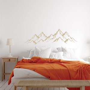May include: A white bed with an orange blanket and two white pillows. A mountain range silhouette decal is on the wall behind the bed.