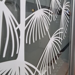 May include: White decorative window film with a design of stylized fern leaves. The film is applied to a glass window.