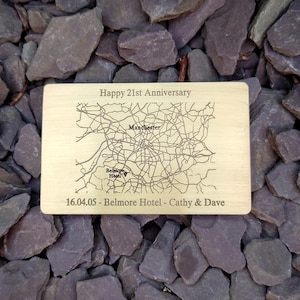 May include: A rectangular light-colored wooden plaque featuring an engraved map of Manchester, England. The text reads Happy 21st Anniversary, Manchester, Belmore Hotel, and 16.04.05 - Belmore Hotel - Cathy & Dave, with a location pin icon.
