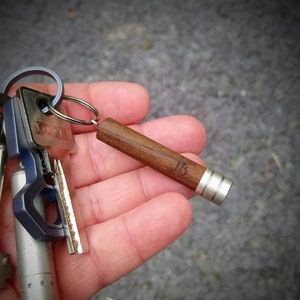 May include: A keychain with a wooden stick attached to it. The stick has a silver cap on one end and the letters "JB" engraved on the side. The keychain also has a silver key ring with several keys attached to it.