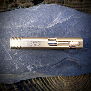 Può includere: Una penna in metallo dorato con una presa testurizzata e l'iscrizione "SWS" sul lato.