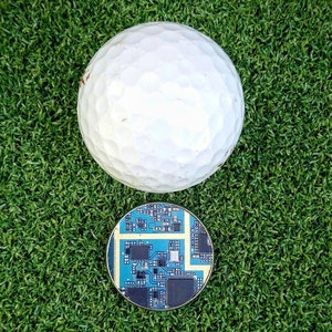 May include: A white golf ball and a blue circuit board on a green artificial grass surface.