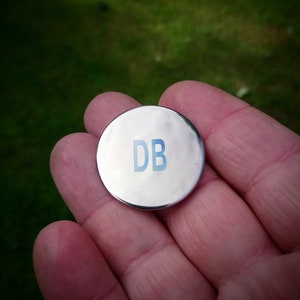 May include: A silver metal disc with the letters "DB" printed in blue.