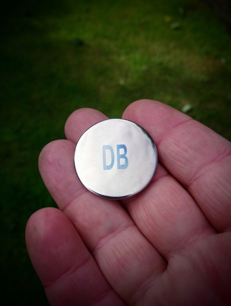 May include: A silver metal disc with the letters "DB" printed in blue.