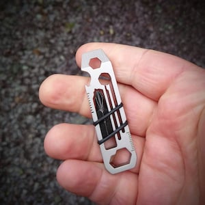 May include: A silver multi-tool with a bottle opener, screwdriver, and wrench. The tool is held in a hand.