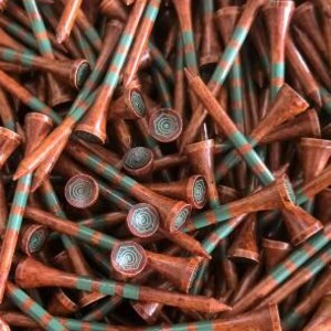 May include: A pile of brown golf tees with green stripes. The tees have a decorative, circular design on the top.