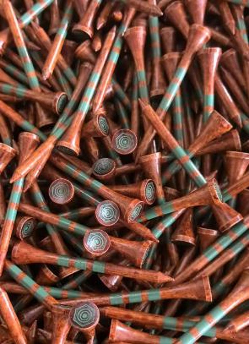 May include: A pile of brown golf tees with green stripes. The tees have a decorative, circular design on the top.
