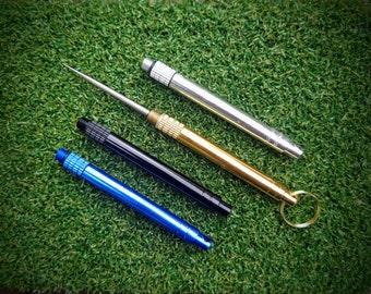 May include: Four different colored metal tools with a pointed tip and a keyring on one of the tools. The tools are on a green artificial grass surface.