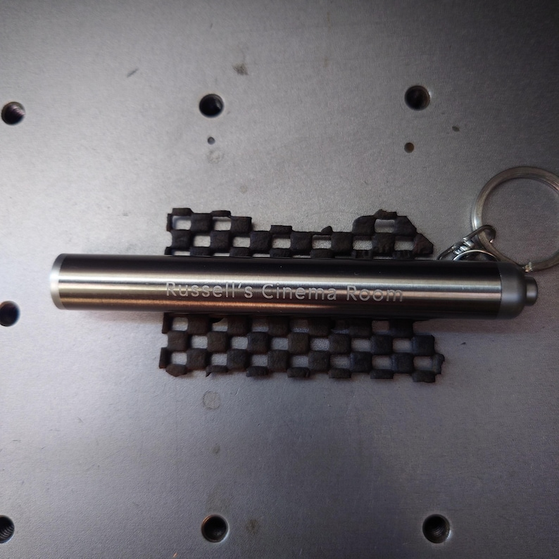Pu&ograve; includere: Un portachiavi in metallo color argento con la scritta incisa "Russell's Cinema Room". Il portachiavi include una torcia cilindrica e un elemento di design nero a scacchi. &Egrave; presente un portachiavi argentato.