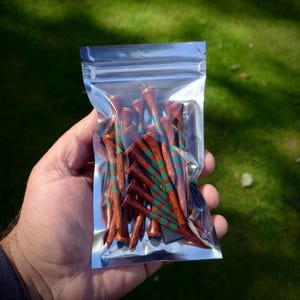 May include: A clear plastic bag filled with wooden golf tees. The tees are brown with green and red stripes.