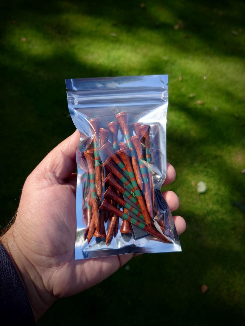 May include: A clear plastic bag filled with wooden golf tees. The tees are brown with green and red stripes.