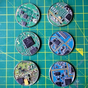 May include: Six round, green and blue circuit boards with gold-colored components. The circuit boards are arranged in a circle on a green grid.