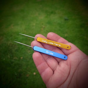 May include: Two small tools with pointed ends, one gold and one blue. The gold tool has the text "Wally was here" engraved on it. The blue tool has the text "Birdie" engraved on it.