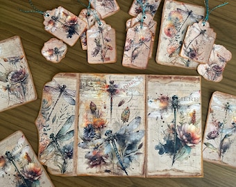 May include: A set of vintage-style paper tags featuring dragonfly illustrations and floral designs. The tags are printed on textured paper with a distressed look and have a rustic brown color scheme. The text on the tags includes French words and phrases.