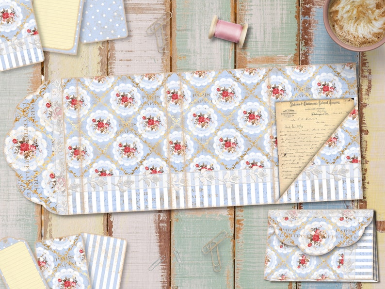 May include: A blue and white patterned paper envelope with a gold trim and a floral design. The envelope is open and a letter is visible inside. The letter is written in cursive and has a blue and white patterned border. The envelope is on a wooden surface with a cup of coffee and a spool of thread.