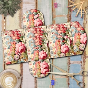 May include: A floral-patterned paper craft project, featuring a box design with a vintage rose and floral print in shades of pink, red, and blue. Scissors and a cup of coffee are placed nearby. The craft project is partially assembled.