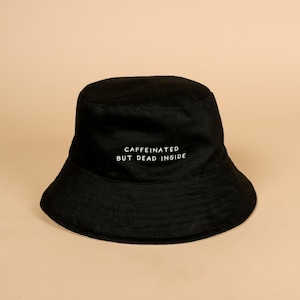 Puede incluir: Sombrero de cubo negro con el texto "caffeinated but dead inside" bordado en blanco.