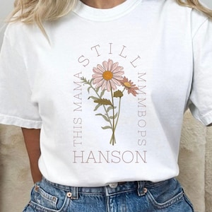 May include: White t-shirt with a floral design and the text "This Mama Still MmmBops Hanson".