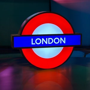 Peut inclure: Un panneau de m&eacute;tro londonien rouge et bleu avec le mot "LONDON" en lettres blanches.