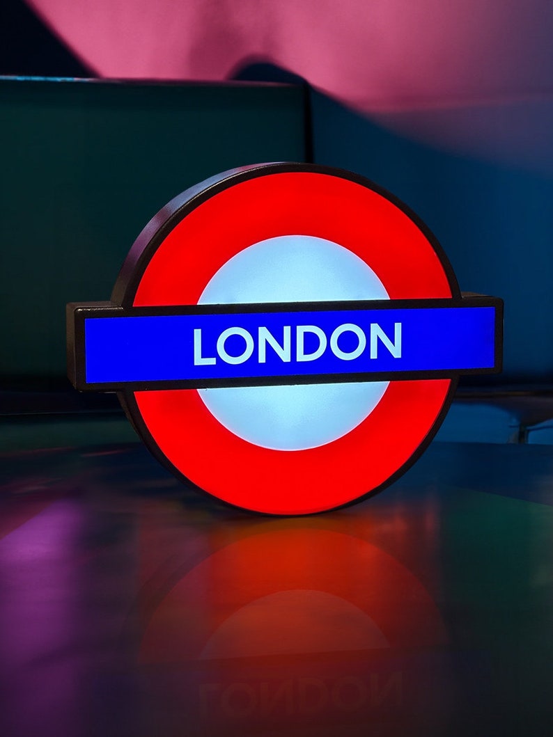 Peut inclure: Un panneau de m&eacute;tro londonien rouge et bleu avec le mot "LONDON" en lettres blanches.