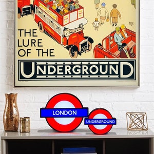 Peut inclure: Deux panneaux du m&eacute;tro londonien, l'un avec le mot "LONDON" et l'autre avec le mot "UNDERGROUND". Les deux panneaux sont rouge, blanc et bleu et ont une forme circulaire avec une bordure noire.