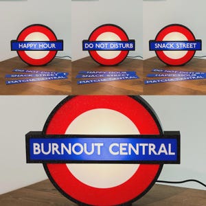 May include: A circular light-up sign featuring a red ring and a horizontal blue bar with interchangeable text inserts. The inserts display phrases including HAPPY HOUR, DO NOT DISTURB, SNACK STREET, MATCHA CENTRAL, and BURNOUT CENTRAL in white capital letters.
