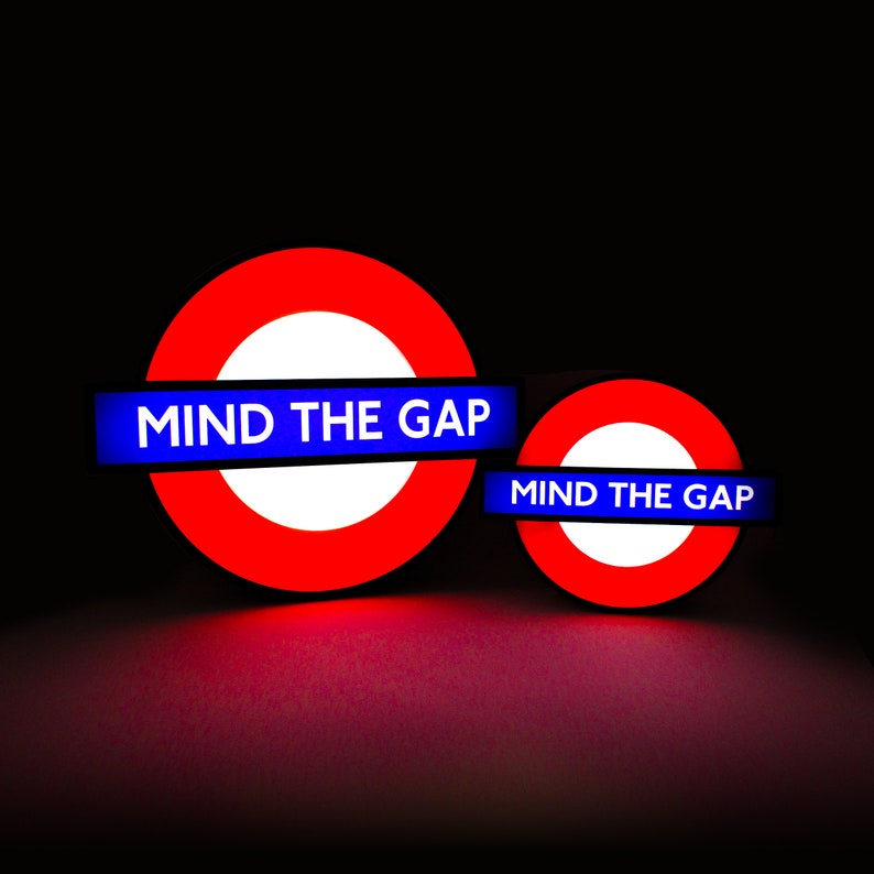 Peut inclure: Deux panneaux du m&eacute;tro londonien rouge et blanc avec du texte bleu qui dit "MIND THE GAP".