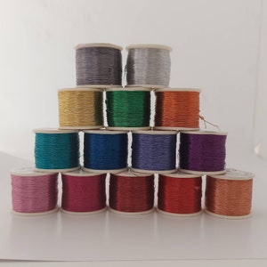 May include: A collection of 12 spools of metallic thread in various colors, including gold, silver, green, blue, purple, red, and pink. The spools are arranged in a pyramid shape.