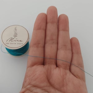 May include: A spool of teal coloured thread with a label that reads "Mira The Earth Store" on a white background.