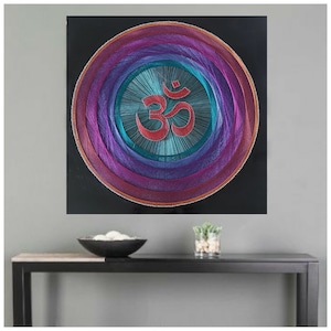 May include: A colorful string art wall hanging with a circular design featuring the Om symbol in red. The background is black.