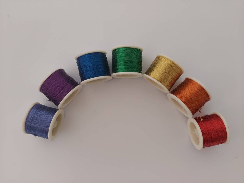 May include: Eight spools of thread in different colours arranged in a semi-circle. The colours are blue, purple, green, gold, orange, and red.