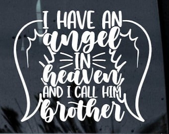 May include: A white vinyl decal applied to a dark window, featuring stylized angel wings framing the text I HAVE AN angel IN heaven AND I CALL HIM brother in a combination of bold block lettering and a decorative cursive script font.