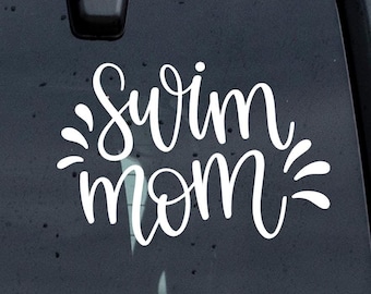 May include: White vinyl decal with the text "Swim Mom" in a cursive font. The text is surrounded by a stylized sunburst design.