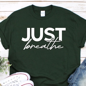 以下が含まれることがあります： 白い文字で「JUST breathe」と書かれた濃い緑色のTシャツです。