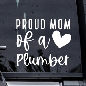 May include: White vinyl decal with the text "Proud Mom of a" followed by a white heart and the text "Plumber".