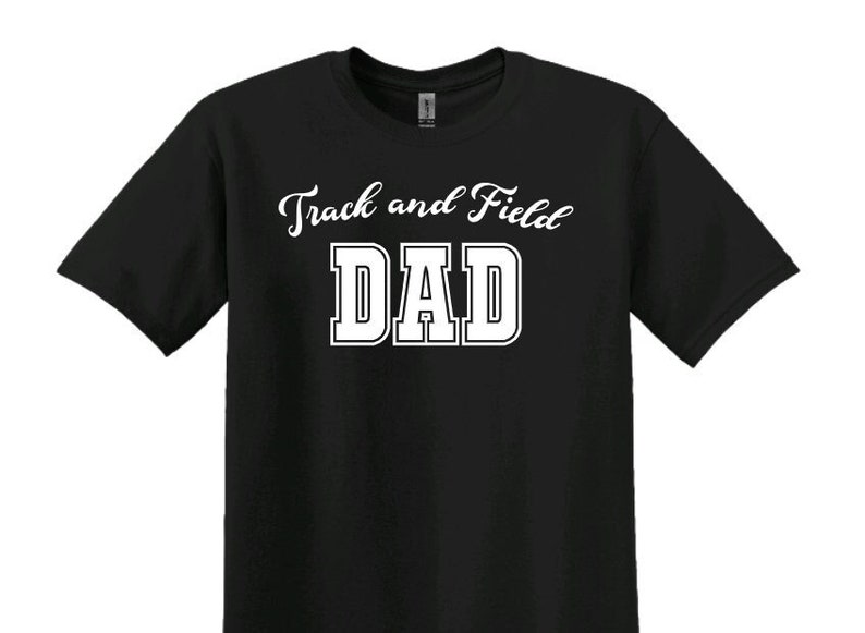 Może przedstawiać: Czarny T-shirt z białym tekstem, kt&oacute;ry brzmi "Track and Field Dad" w sportowym kroju.